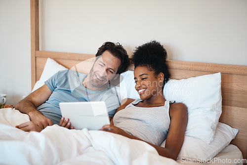 Image of Happy couple, tablet and relax on bed for entertainment, movie or online streaming together at home. Interracial man and woman relaxing, morning or watching on technology or social media in bedroom