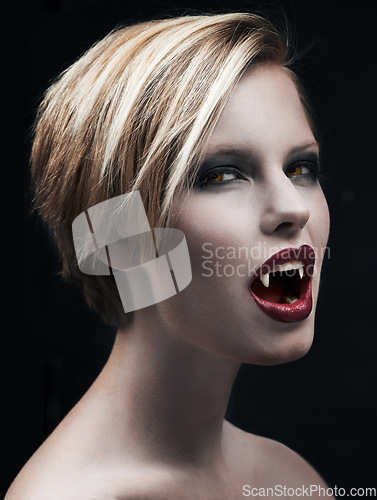 Image of Portrait, fangs and female vampire in studio on dark background for halloween or cosplay. Fantasy, horror or scary with attractive young woman monster posing as an evil villain with creative makeup