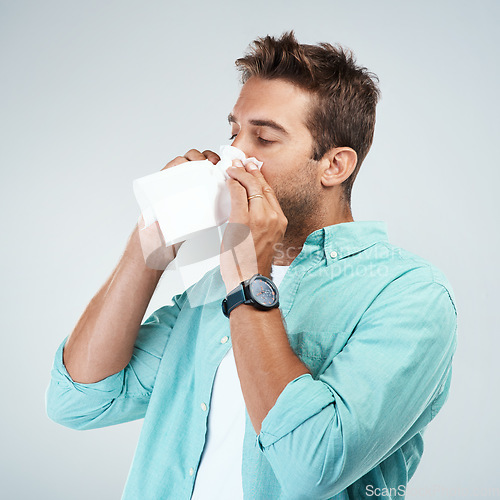 Image of Blowing nose, tissue and man in studio with allergy, sickness and virus infection on white background. Health, wellness and face of male person with handkerchief for hayfever, cold and sneeze for flu