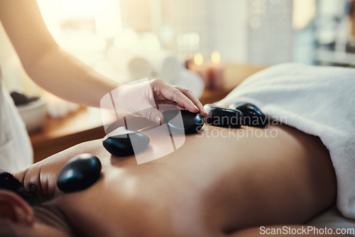 Image of Woman, hands and rocks for back massage at spa in beauty relaxation or skincare on bed. Hand of masseuse applying hot rock or stones on female for physical therapy, zen or skin treatment at resort