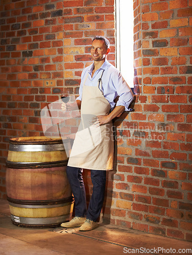 Image of Portrait, man sommelier with glass and taste in cellar or factory. Alcohol or drink, production storage or industry and happy mature male smile and standing by wooden barrel during wine tasting