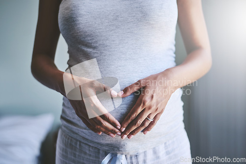 Image of Pregnant woman with a heart shape on her belly for love, care and maternity in her house. Bonding, maternal and closeup of a female person holding her pregnancy stomach for motherhood at her home.