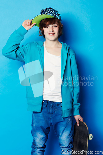 Image of Fashion, skateboard and portrait of a child in a studio with a casual, trendy and cool outfit. Skateboarder, smile and happy boy kid model with skating style posing isolated by a blue background.