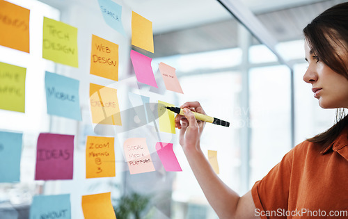 Image of Woman writing notes, brainstorming with ideas on glass board and sticky note, planning in office with focus. Creative project, agenda and female employee working, strategy and storyboard with goals