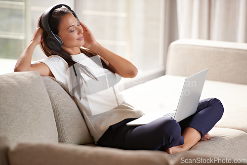 Image of Headphones, laptop and woman on a home sofa listening to music or audio while streaming online. Calm female person relax on couch to listen to radio or song with internet connection and technology