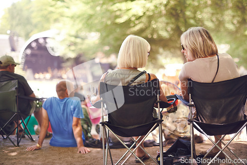 Image of Back, friends sitting and outdoor festival on camping chair, talking and women in audience, concert or music performance. People, fans relaxing together or summer show, entertainment or culture event