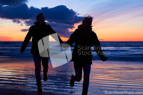 Image of Sunset, silhouette and couple running at beach on romantic date, vacation or holiday in nature. Man and woman holding hands with love and care on travel, adventure or trip with clouds, sky and ocean