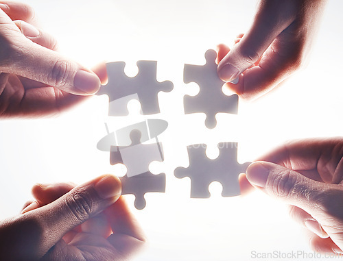 Image of Hands, puzzle and flare with a business team working together on project planning closeup from below. Teamwork, collaboration or synergy and employee group with a jigsaw for strategy or innovation