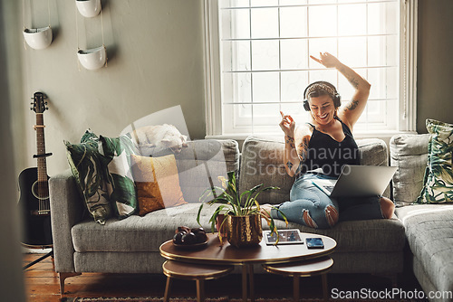 Image of Dancing, headphones and woman on sofa and laptop, happy energy and mental health music in her home. Young person on couch listening to audio tech, electronics and podcast on computer in living room