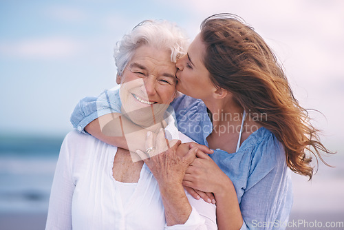 Image of Woman, kiss and senior mother at beach with happiness, love and smile for mothers day on vacation. Elderly lady, daughter and happy with hug, bonding and outdoor by ocean for holiday in retirement