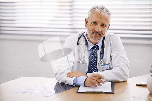 Image of Happy, portrait and doctor with a clipboard in his office analyzing test results in a hospital. Confidence, smile and professional mature male healthcare worker sitting by his desk in medical clinic.