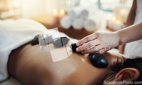 Image of Woman, hands and rocks in back massage at spa for skincare, beauty or relaxation on bed indoors. Hand of masseuse applying hot rock or stones on female for physical therapy or treatment at resort