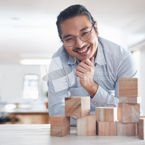 Image of Design, strategy and portrait of man with building blocks in office, thinking and innovation for balance with smile. Engineering, challenge and asian designer with wood block game for problem solving