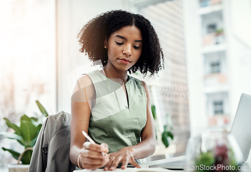 Image of Corporate, black business woman writing in book and at laptop sitting at desk in her office. Planning schedule, reminder and focused African female worker in workplace write notes on information