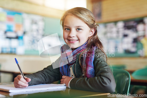 Image of Education, portrait of young girl in classroom and writing in her notebook at her desk in school building. Studying or homework, learn or academic and happy female student with pen sitting on chair