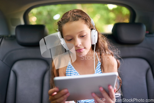 Image of Technology, young girl in car with tablet and headphones while travelling. Social media or streaming, internet connectivity and child on road trip on vacation in vehicle with digital or mobile device