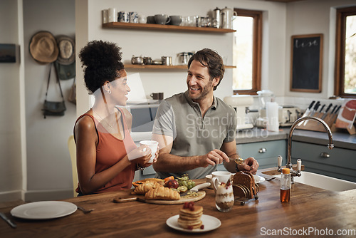 Image of Happy interracial couple, breakfast and morning in kitchen for healthy meal, talk or bonding at home. Man and woman smiling for coffee, conversation or tea and food on weekend together by the table