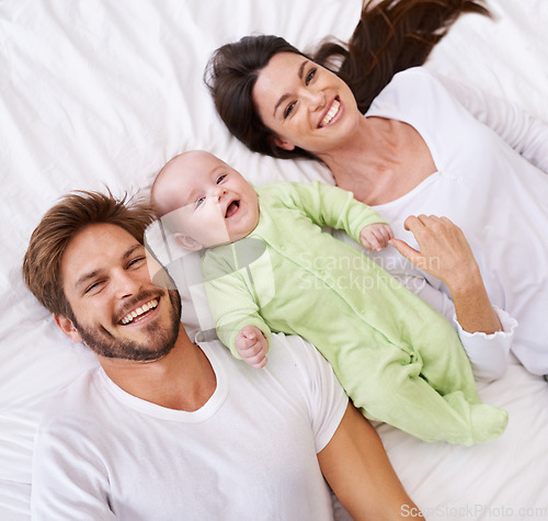 Image of Above, portrait and happy parents with baby on bed for love, care and quality time together at home. Smile of mother, father and family with cute newborn kid relax in bedroom, support and happiness