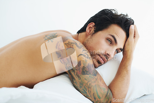 Image of Thinking, relax and sexy with a topless man on a bed, lying in studio on a white background. Tattoo, idea and shirtless with a handsome young male model posing in a bedroom for sensuality or desire