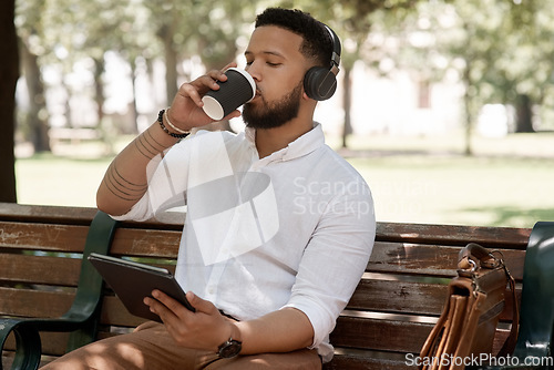 Image of Business man, coffee and headphones outdoor with a tablet on a park bench for a break with internet. Male entrepreneur person in nature while streaming and listening to music on a audio app to relax