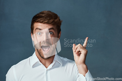 Image of Portrait, wow and idea with a man pointing in studio on a blue background during a lightbulb moment. Face, surprise and eureka with an excited young male person looking shocked or amazed by good news