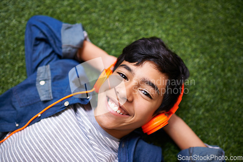 Image of Boy child, grass and lying with headphones in portrait for music, streaming and online audio with happiness. Male kid, happiness and listening to sound, internet radio or podcast on lawn in garden