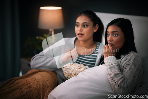 Image of Popcorn, eating and people or friends with horror movies, scary show and sleepover on bed, streaming service or television. Gen z women relax in bedroom for drama TV film, home cinema or subscription