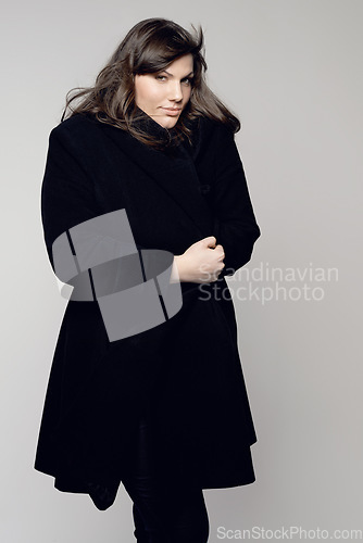 Image of Woman, fashion and portrait of plus size model posing in winter clothing against a grey studio background. Isolated female person standing with stylish black coat, body or warm fashionable clothes