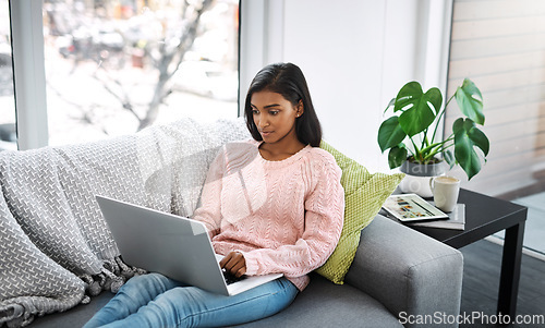 Image of Woman, laptop and typing on home sofa for student research, streaming or social media. Indian female person on a couch to relax, surfing internet or writing email for communication on website