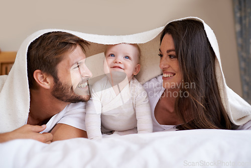 Image of Happy family, parents and baby with blanket on bed for love, care and quality time together. Mother, father and playful newborn child relaxing in bedroom with bedding fort, smile and bonding at home