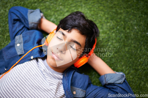 Image of Headphones, music and boy relax on grass with eyes closed outdoors on holiday, free time and weekend. Calm, peace and face of kid in garden listening to song, track and streaming audio for happiness