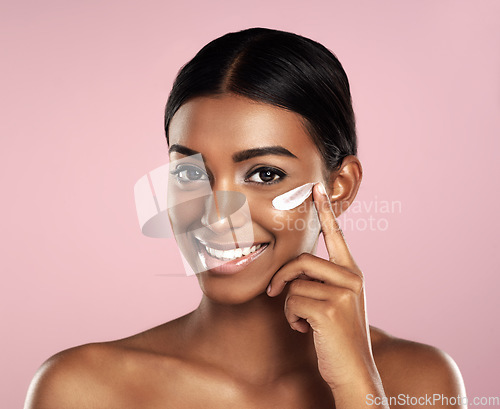 Image of Happy, skincare and face of woman with cream in studio isolated on a pink background. Dermatology, creme cosmetics and portrait of happy Indian female model apply moisturizer lotion for healthy skin.