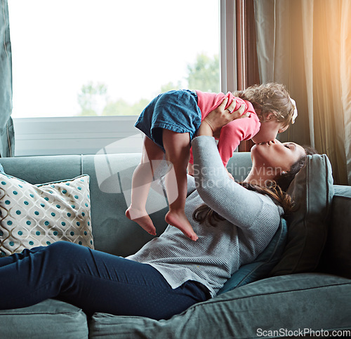 Image of Mom, kiss and lifting girl on sofa in home living room and relax, bonding and quality time together or mother, love and family happiness. Child, mommy and playing game on couch in house with smile