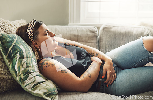 Image of Period, menstrual pain and a woman on a sofa in the living room of her home with cramps of the abdomen. Stomach, digestion or menstruation with a young female person holding her belly in discomfort