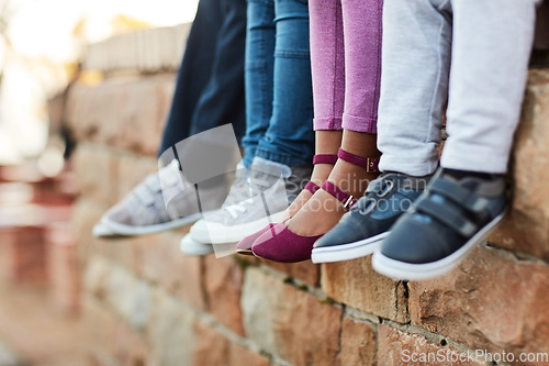 Image of Shoes, legs of school children and sitting on brick wall together. Group of friends, friendship and young student outside of classroom during lunch period or break time with footwear showing.