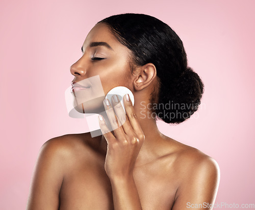Image of Skincare, beauty and woman with cotton pad on face, smile and makeup removal with luxury skin product in studio. Dermatology, facial cleansing cosmetics and happy model isolated on pink background.