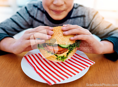 Image of Child, hands and eating burger on table for delicious lunch, meal or food with healthy vegetables at home. Hand of hungry little boy holding beef hamburger for fresh dinner, nutrition or vitamins