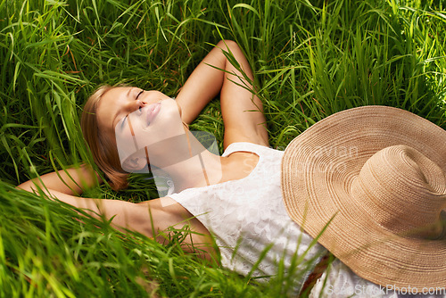 Image of Young woman, sleep and green grass or girl smile in nature, field or countryside break for relax in summer sun. Happy female person, hat and sleeping in spring garden or resting hands behind head