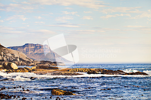 Image of Mountains, ocean and nature with waves at beach for environment, landscape and blue sky. Calm, summer and seascape with sunrise on horizon at coastline for tropical, clouds and water on rock surface