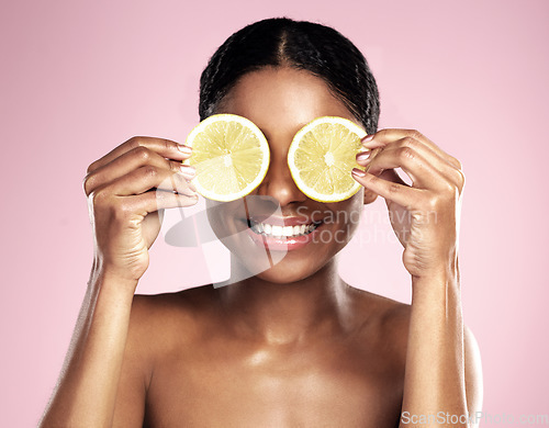 Image of Happy woman, beauty and eyes with lemon in studio, pink background and vitamin c benefits. Face, african model and fun with citrus fruits for natural skincare, vegan cosmetics and facial aesthetic