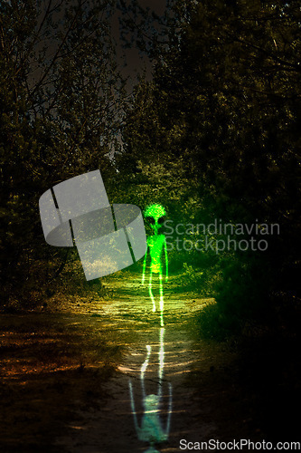 Image of Alien, night and creature walking for horror, fantasy or graphic design in nature, forest or planet earth of green glow. Science fiction, silhouette or scary extraterrestrial in dark or outdoor woods