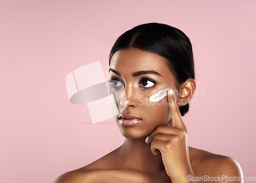 Image of Thinking, skincare and face of woman with cream in studio isolated on a pink background mockup. Dermatology, creme cosmetics and serious Indian female model apply moisturizer lotion for skin health.
