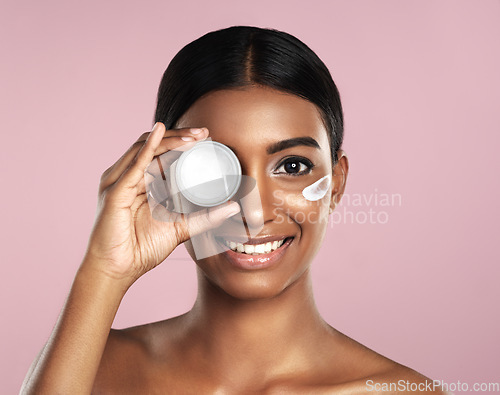 Image of Face, skincare and woman with cream container in studio isolated on a pink background. Portrait, dermatology cosmetics and happy Indian female model with lotion, moisturizer product or beauty creme.