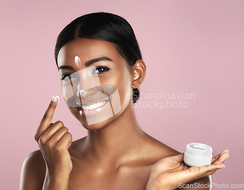 Image of Skincare, face and woman with cream container in studio isolated on a pink background. Product, dermatology creme and portrait of happy Indian female model apply lotion, moisturizer and cosmetics.