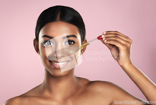 Image of Face, skincare serum and happy woman in studio isolated on a pink background. Portrait, cosmetics and Indian model with hyaluronic acid, essential oil or vitamin c dropper for healthy dermatology.