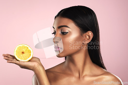 Image of Face, skincare and woman looking at an orange in studio isolated on a pink background. Fruit, natural cosmetics and Indian female model holding food for healthy diet, nutrition or vitamin c to detox.
