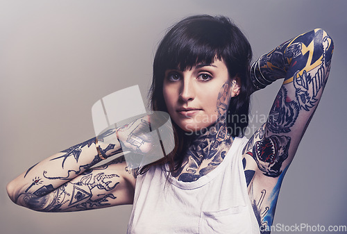 Image of Portrait, tattoo and edgy with a woman in a tank top on a studio gray background for contemporary style. Fashion, body art and punk with an attractive young female model posing to show her ink