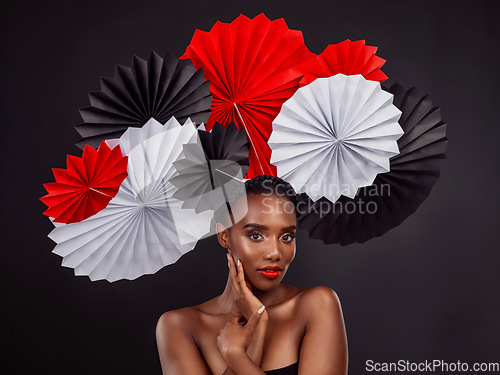 Image of Beauty, portrait and black woman with origami fans in studio isolated on a dark background. Serious face, makeup cosmetics and skincare of female model with traditional Japanese paper art for culture