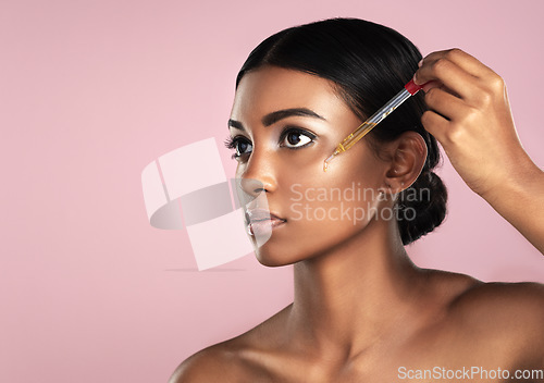 Image of Face, skincare serum and serious woman in studio isolated on a pink background mockup. Dermatology, cosmetics and Indian model with hyaluronic acid, essential oil or vitamin c dropper for skin health