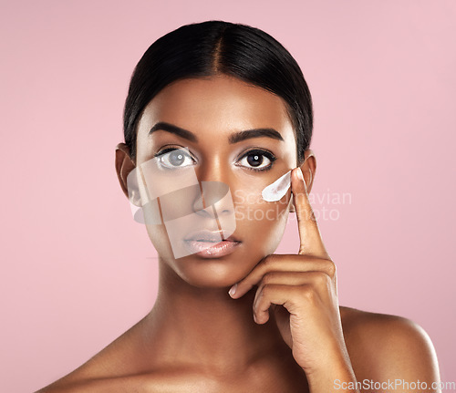 Image of Portrait, skincare and face of woman with cream in studio isolated on pink background. Dermatology, creme cosmetics and serious Indian female model apply moisturizer lotion for skin health or beauty.